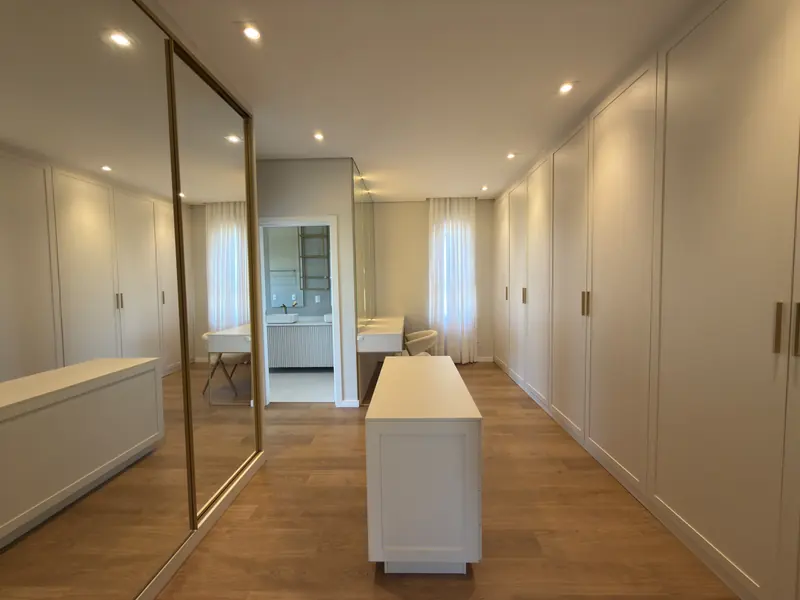 Closet da suíte master com ilha e portas espelhadas